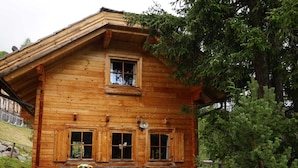 A wooden cabin with a porch, a bench, and a chair.