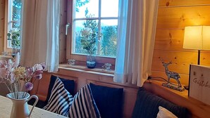 A cozy room with a wooden interior, a window with curtains, a vase with flowers, and a lamp on the right side.