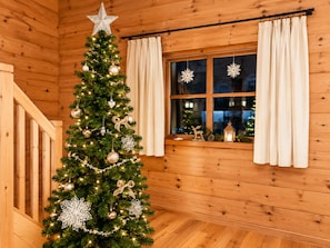 A Christmas tree in a wooden cabin with a star on top, curtains on the window, and a wooden staircase. - Chalet Bergliebe Turrach (Stadl-Predlitz)