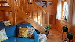 A cozy cabin interior with a wooden staircase, a blue sofa with decorative pillows, and framed pictures on the walls.