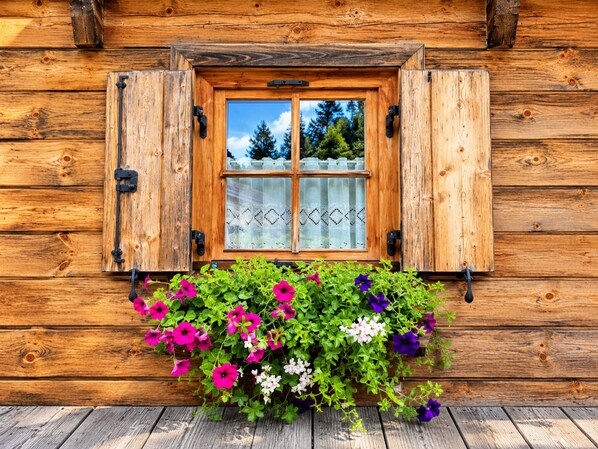 A wooden cabin with a window featuring a decorative curtain and a flower box with various flowers. - Chalet Bergliebe Turrach (Stadl-Predlitz)