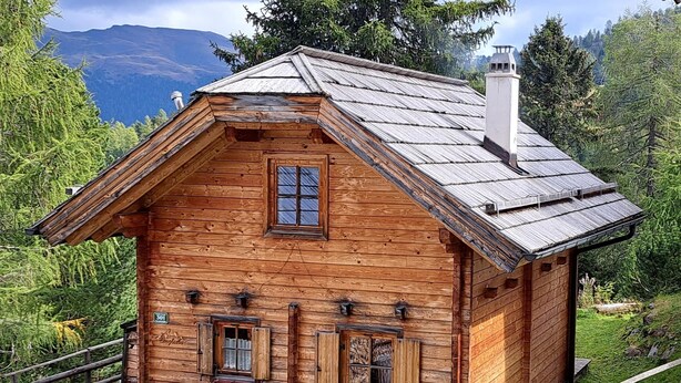 A wooden cabin with a sloped roof, a front porch, and a chimney.