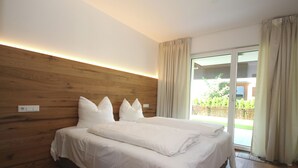 Un dormitorio moderno con cabecera de madera, una cama grande con ropa de cama blanca y un ventanal corredero que da a un espacio exterior.