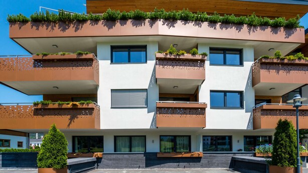 Un edificio moderno de varios pisos con balcones, ventanas amplias y macetas exteriores.