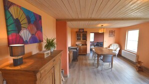 Een ruime woonkamer met een houten eettafel, stoelen, een bank en een keuken op de achtergrond.