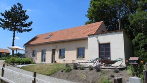Een gelijkvloers huis met een rode dakbedekking, een veranda en een tuin vol planten en bloemen.