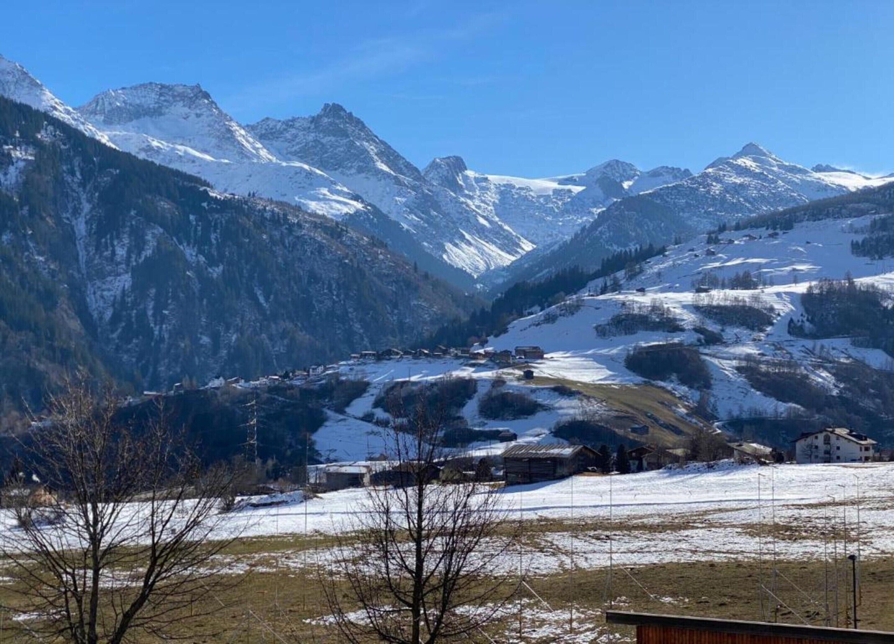 A mountainous landscape with snow-covered peaks and a valley with buildings.