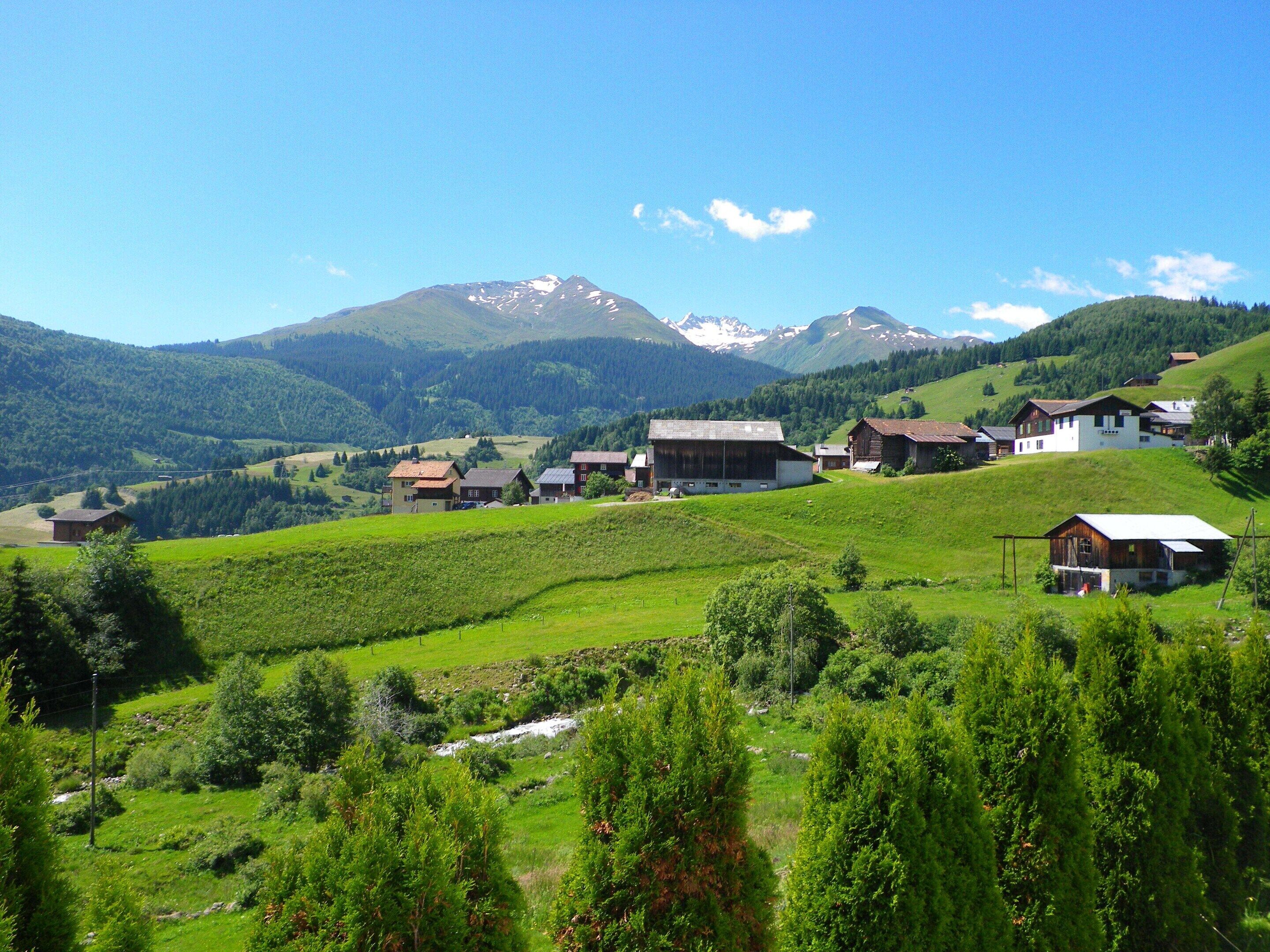 A rural village with traditional houses, a mountain backdrop, and a clear sky.