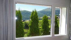 Ein Zimmer mit großem Fenster und Blick auf eine Berglandschaft mit Bäumen und Häusern.