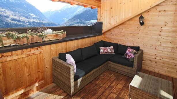 Un interno in legno con un divano modulare nero, una panca di legno e una finestra che si affaccia su un paesaggio montuoso.
