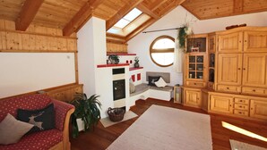 Un accogliente soggiorno con soffitto in legno, un divano rosso con motivi decorativi, un'ampia finestra e mobili contenitori in legno a muro.