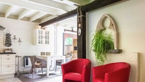 A modern kitchen with white cabinets, a dining area with wicker chairs, and a red chair in the foreground. - Charming Retreat, Veldegem (Zedelgem)