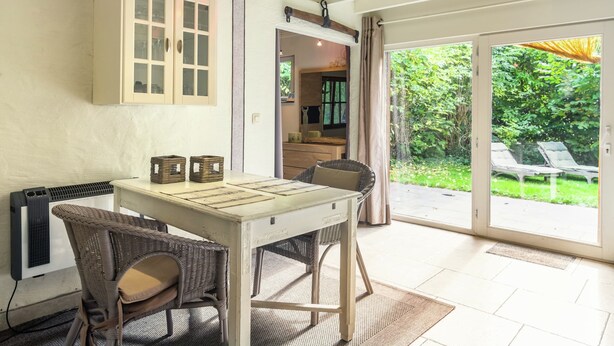 A dining area with a table and chairs, a cabinet, and a view of the garden through a glass door. - Charming Retreat, Veldegem (Zedelgem)