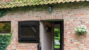 A brick building with a wooden door, a window with a shutter, and a hanging flower basket. - Charming Retreat, Veldegem (Zedelgem)