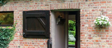 A brick building with a wooden door, a window with a shutter, and a hanging flower basket.