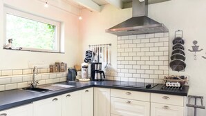 A modern kitchen with white cabinets, a black countertop, a stainless steel range hood, and a window with a view of greenery. - Charming Retreat, Veldegem (Zedelgem)