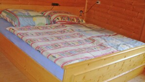 A single bed with a colorful quilt and pillows, wooden headboard, and a brick wall background. - Chalet in Kolbnitz Near Ski Slopes (Reisseck)