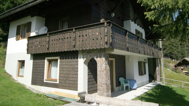 A two-story chalet with a balcony, stone foundation, and a small outdoor seating area. - Apartment at Nassfeld in Carinthia (Hermagor-Pressegger See)