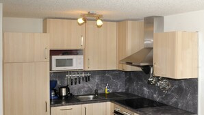 A compact kitchen with wooden cabinets, a black marble countertop, a microwave, a knife block, and an oven. - Apartment at Nassfeld in Carinthia (Hermagor-Pressegger See)