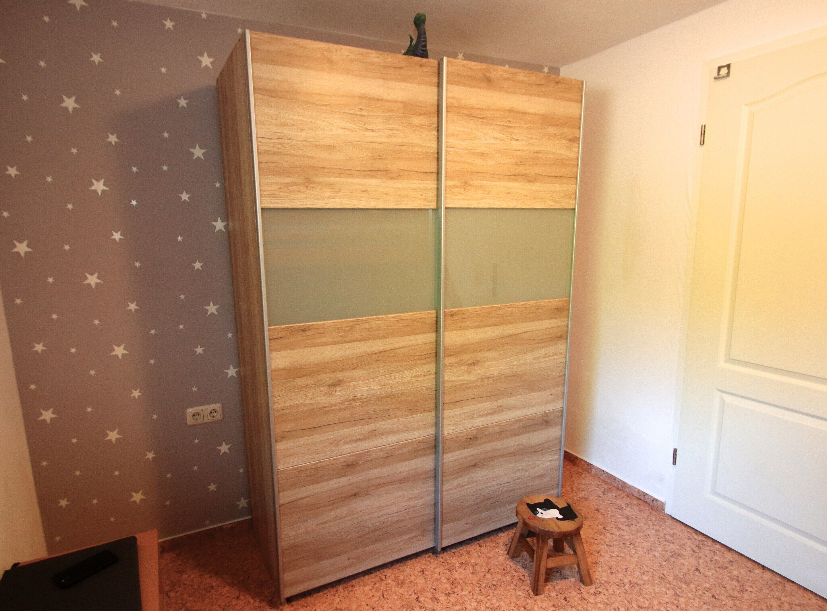 A room with a star-patterned wall, a wooden wardrobe with glass panels, a small stool, and a closed door.