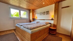 A wooden bed with two pillows, a window, a radiator, a lamp, and a small stool. - Damshagen Kustenkomfort (Damshagen)