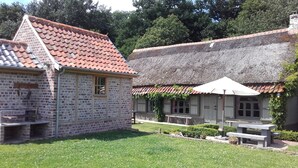 A traditional brick building with a tiled roof, a thatched-roof structure, and a grassy courtyard with a picnic table.