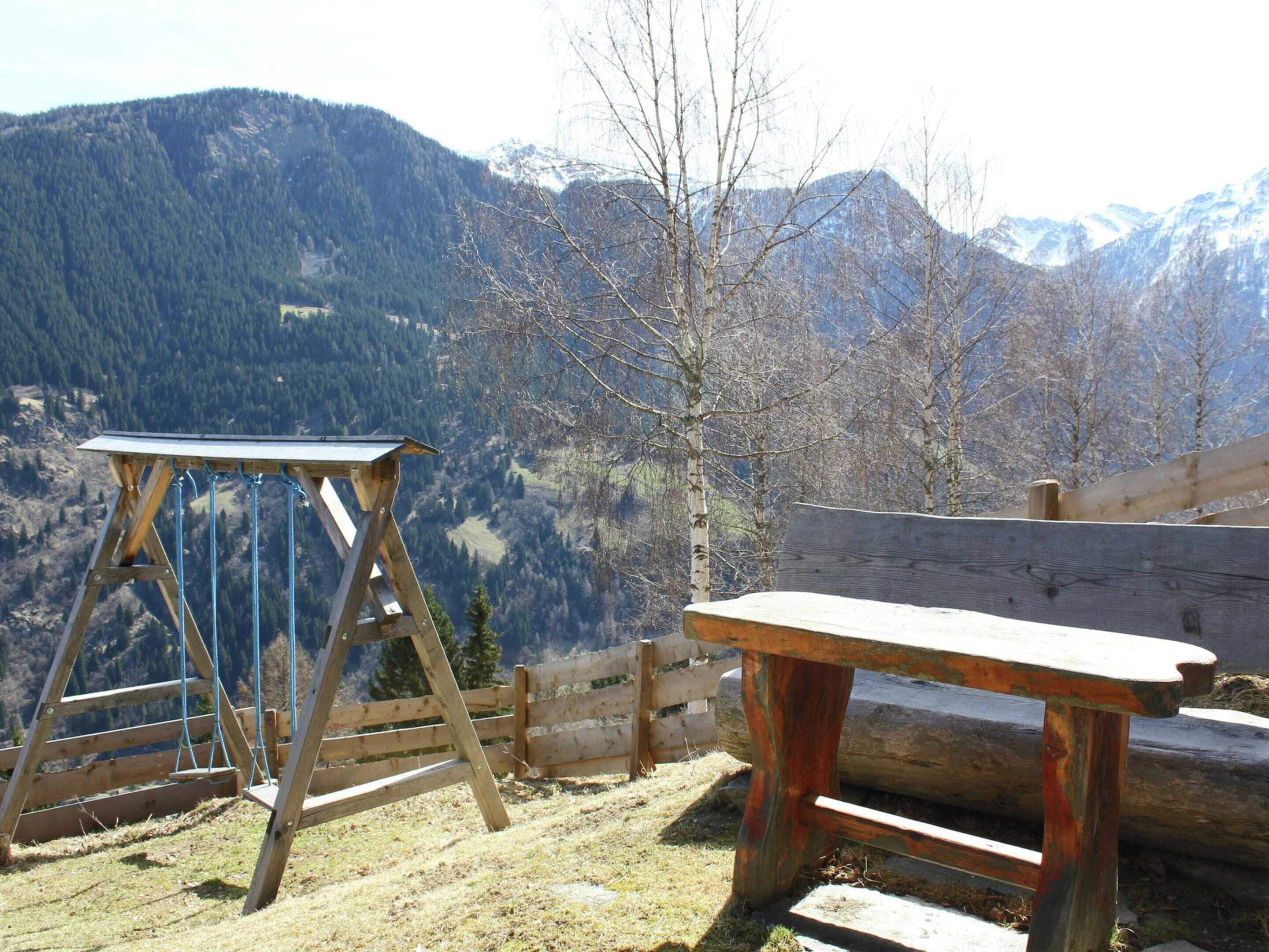 A wooden bench and a wooden table on a hillside with a mountain view in the background.