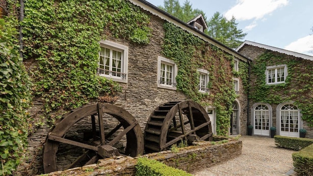 Ein historisches Gebäude mit Steinmauern und Efeu, das große hölzerne Wasserräder und einen Kopfsteinpflasterhof zeigt.