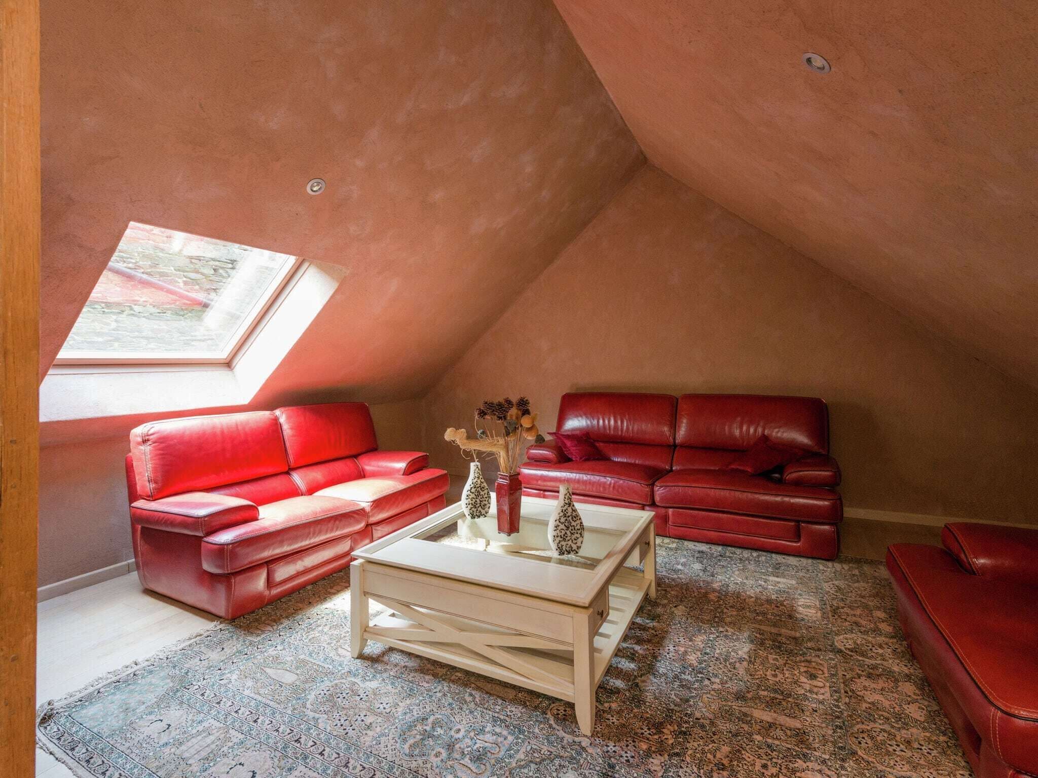 Ein gemütliches Dachzimmer mit roten Ledersofas, einem weißen Couchtisch und einem gemusterten Teppich.