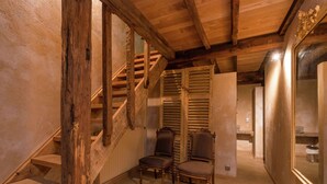 Eine Holztreppe führt zu einer zweiten Etage, begleitet von zwei Sesseln und einem Spiegel.