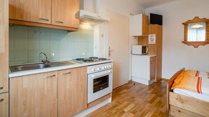 A compact kitchen with wooden cabinets, a sink, a stove, and a microwave. - Holiday Apartment in Tropolach (Hermagor-Pressegger See)