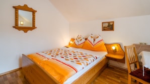 A bedroom with a wooden bed, a nightstand with a lamp, a chair, a small table, a mirror, and a painting on the wall. - Holiday Apartment in Tropolach (Hermagor-Pressegger See)
