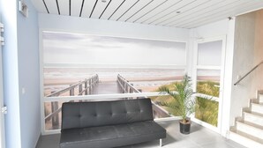 Quarto moderno com grande janela com vista para uma praia, um sofá preto e uma escada.