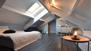 Quarto estilo loft moderno com claraboia, mesa redonda com abajur e escrivaninha com espelho.