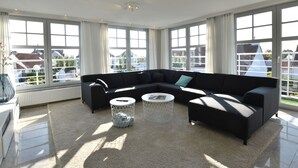 Uma sala de estar moderna com um sofá modular preto, duas mesinhas de centro redondas e amplas janelas com vista para o bairro.