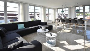 Uma sala de estar moderna com um sofá seccional preto, duas mesinhas de centro redondas e um espaço de jantar com uma mesa de madeira e cadeiras.