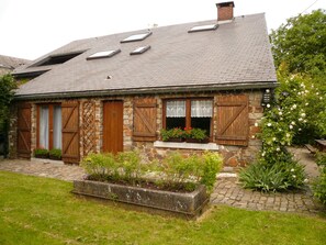 A stone house with a sloped roof, wooden shutters, and a garden with flowers and plants. - Holiday Home in Ronchampay (La Roche-en-Ardenne)