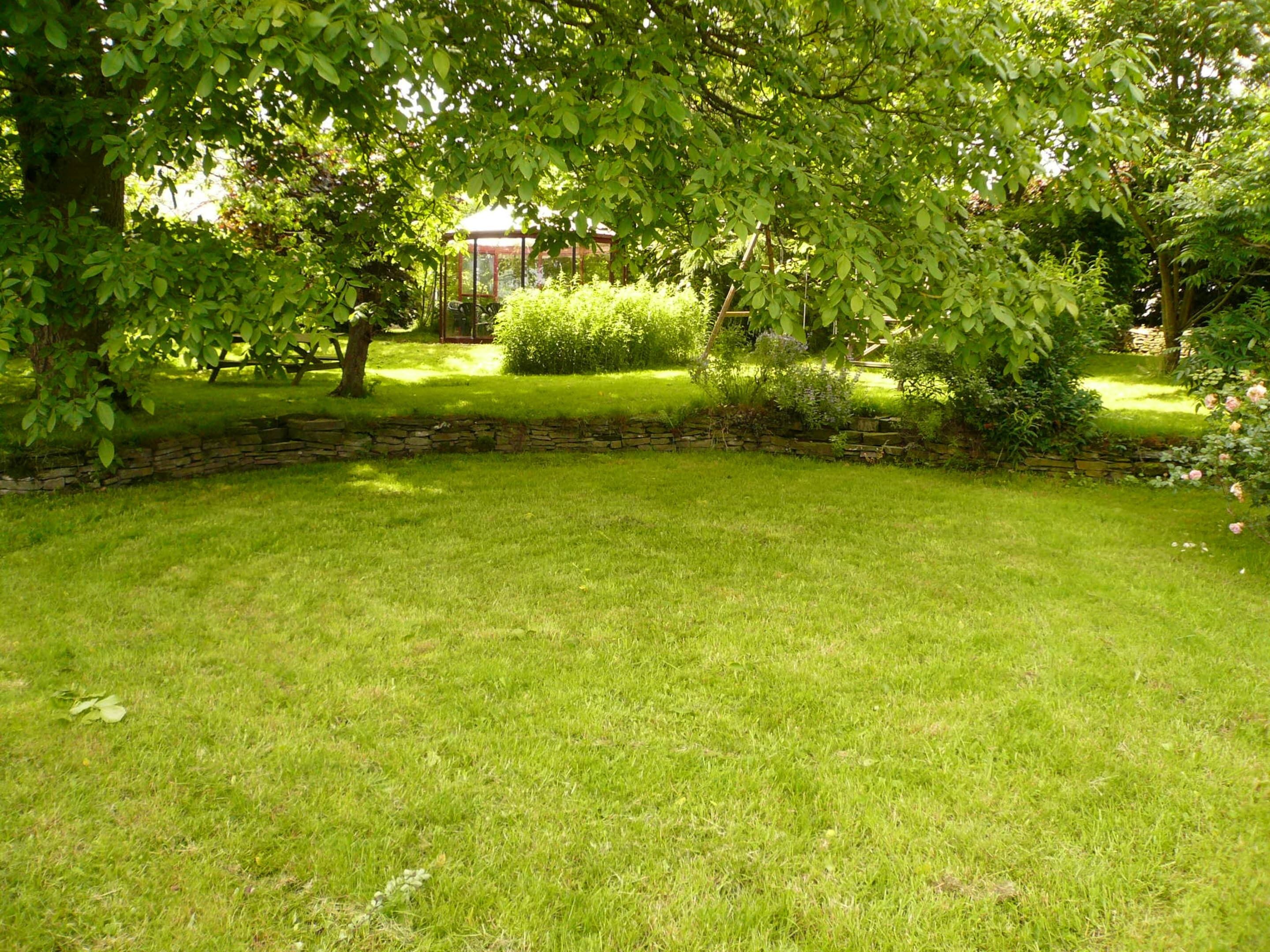 Ein gepflegter Garten mit einer Steinmauer, saftigem Grünrasen und einem Gazebo im Hintergrund.