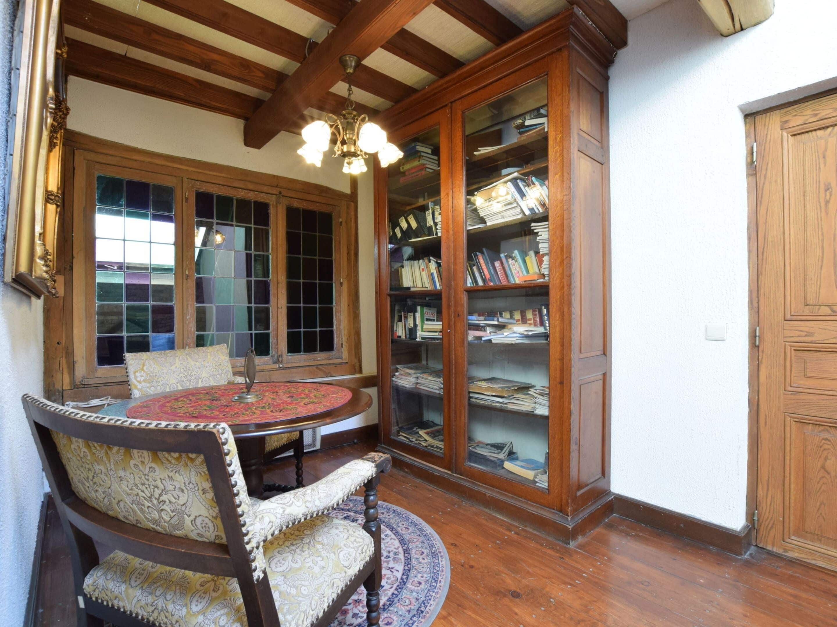 A room with a round table, a wooden chair, a bookshelf, and a wooden cabinet.