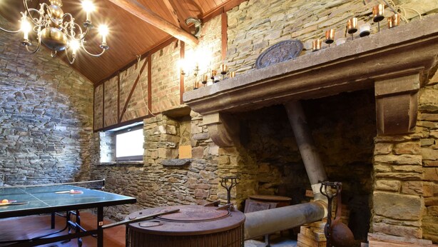 A room with a ping pong table, stone walls, a wooden ceiling, and a stone fireplace with candles. - Holiday Home in Ronchampay (La Roche-en-Ardenne)
