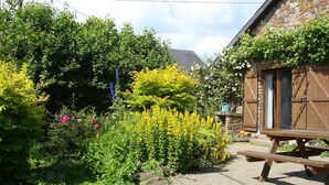 A garden with a stone wall, a wooden bench, and a stone building with wooden shutters. - Holiday Home in Ronchampay (La Roche-en-Ardenne)
