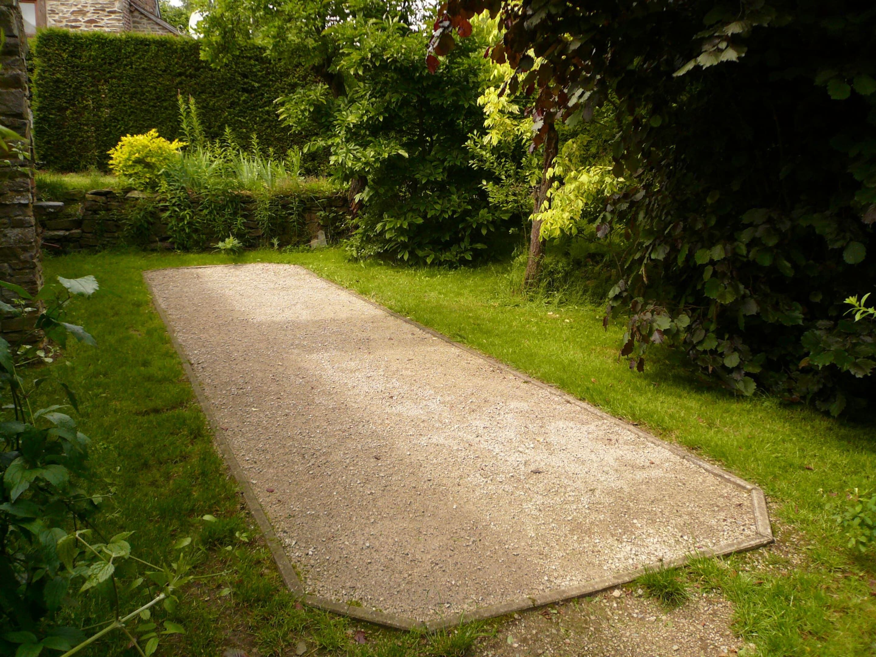A gravel path in a garden with a stone wall and dense foliage.