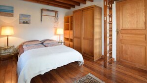 A bedroom with a wooden bed, two bedside lamps, a large wardrobe, and a ladder leading to a loft. - Holiday Home in Ronchampay (La Roche-en-Ardenne)