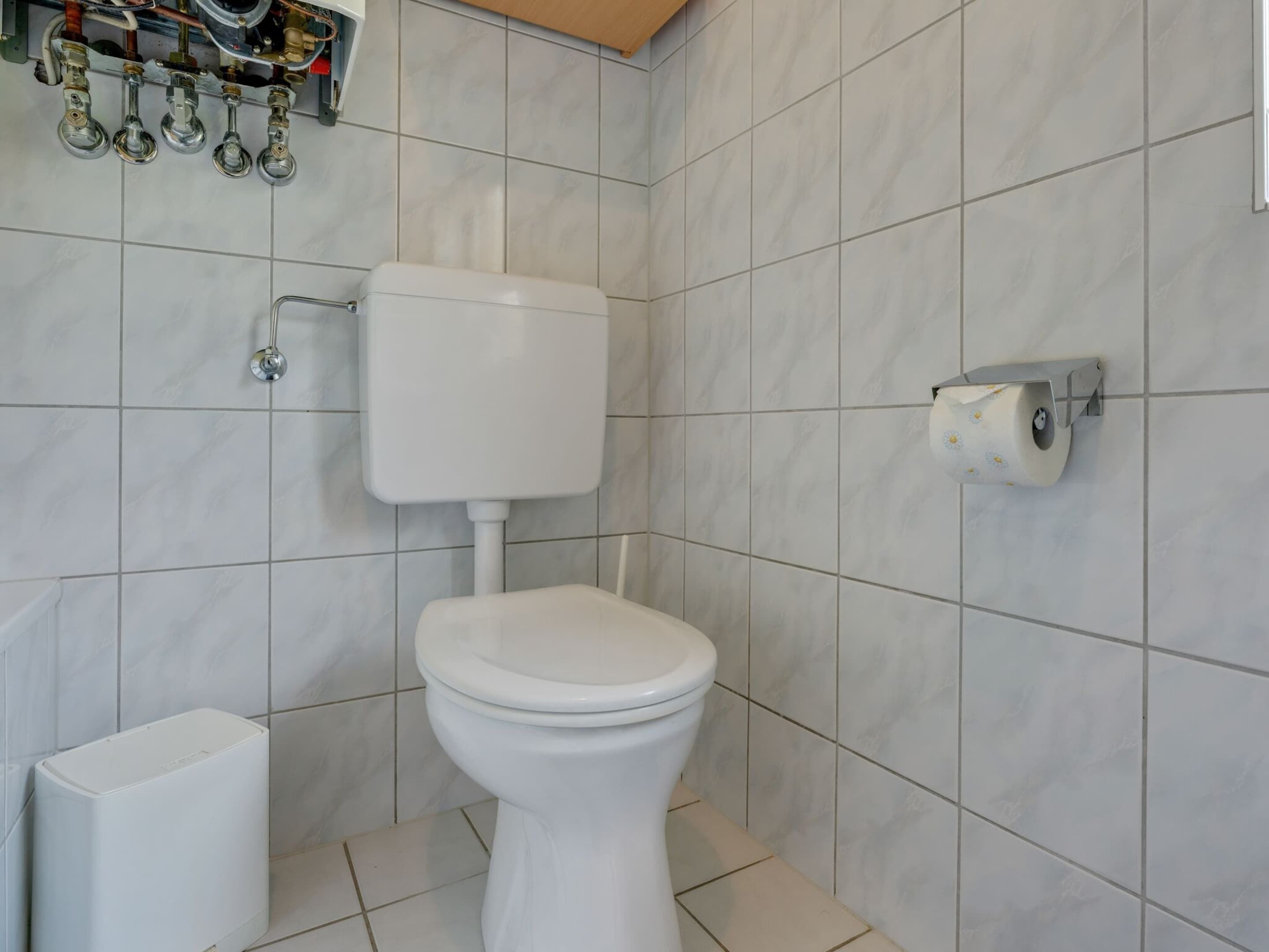A bathroom with a toilet, a bidet, and a toilet paper holder on the wall.