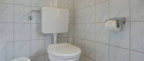 A bathroom with a toilet, a bidet, and a toilet paper holder on the wall.