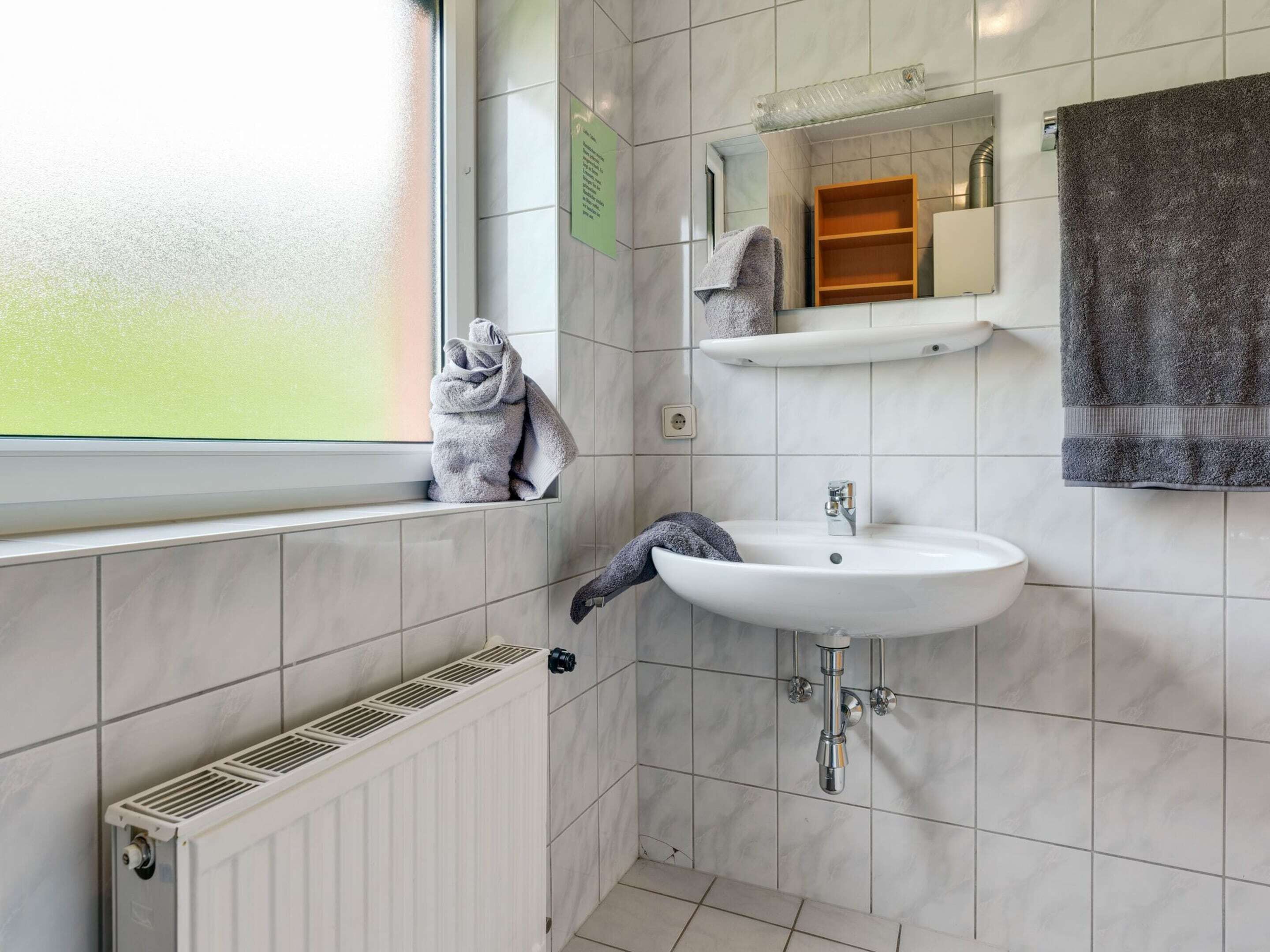 Un baño moderno con un lavamanos blanco, un espejo encima y un perchero para toallas.