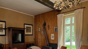 A cozy living room with a fireplace, wooden walls, a sofa, two chairs, a television, and framed pictures on the wall. - Charming Castle in Roumont (Bertogne)