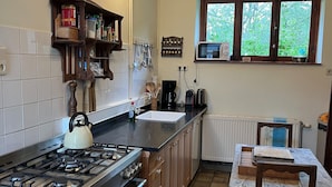 A kitchen with a gas stove, oven, and a kettle. There is a window with a view of greenery outside. - Charming Castle in Roumont (Bertogne)