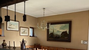 A room with a wooden bench seating area, a table with a white tablecloth, and a chandelier. There are framed pictures on the wall and a painting depicting a landscape. - Charming Castle in Roumont (Bertogne)