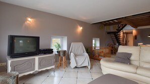 A living room with a television, a white sofa, a covered chair, and a staircase leading to an upper level.